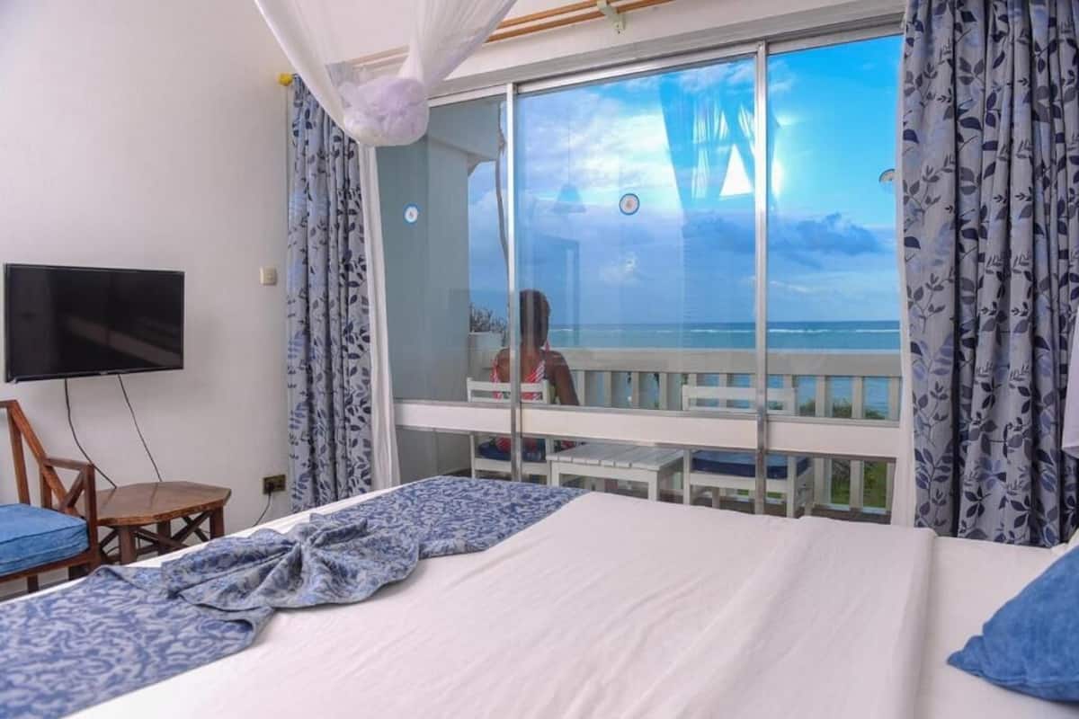 A bedroom with a large bed, a TV, a balcony with a view of the sea, and a table with chairs.