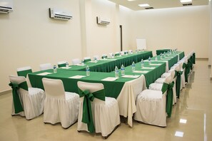 Een congreszaal met lange tafels, stoelen met groene linten en witte stoelen.