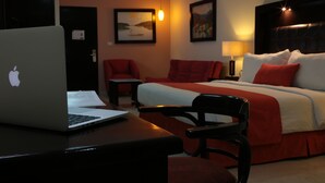 Habitación de hotel con cama, escritorio con ordenador portátil, silla y dos cuadros en la pared.