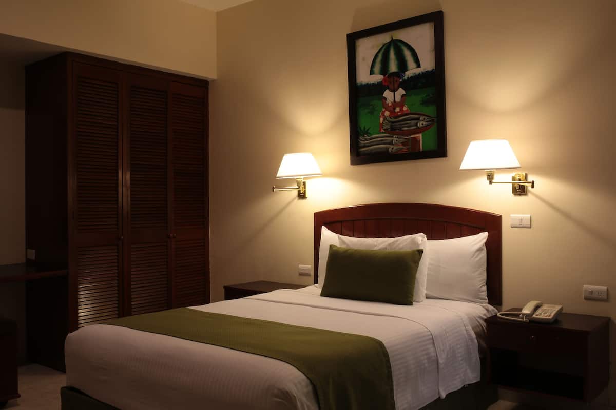 A hotel room with a bed, two bedside lamps, a nightstand, a telephone, and a painting on the wall.
