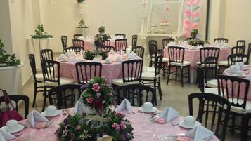 A banquet hall with round tables covered in pink tablecloths, black chairs, and white centerpieces.