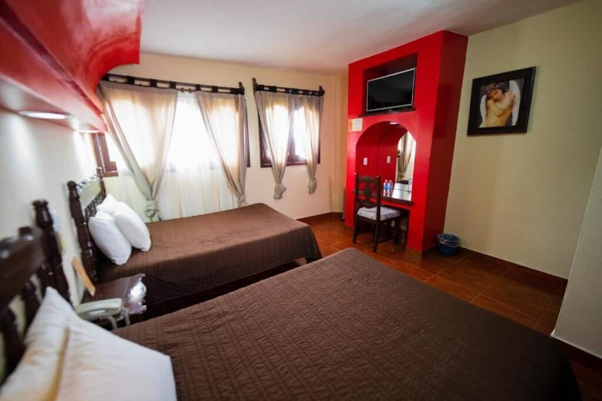 A hotel room with two beds, a desk, a TV, and a red accent wall.