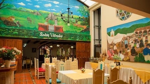A restaurant with a mural of a rural scene and a sign reading "Salon Vitrailes." Tables are set with white tablecloths and wooden chairs. - Hotel D' Monica  (San Cristóbal de las Casas)