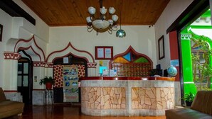 A reception area with a stone counter, a chandelier, and a green exterior view. - Hotel D' Monica  (San Cristóbal de las Casas)