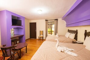 Habitación de hotel con dos camas, un televisor montado en una pared morada, un escritorio de madera y una silla.