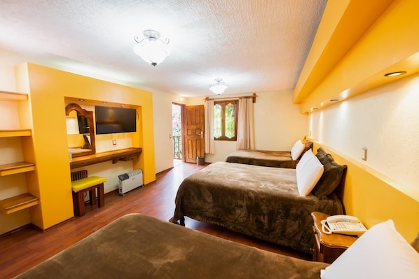 A hotel room with two beds, a desk with a flat-screen TV, a heater, and a small table with a telephone.