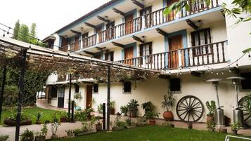Un edificio de dos pisos con balcones, un patio con plantas en macetas y una estructura circular grande.