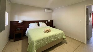 A hotel room with a bed, a nightstand, a lamp, and a ceiling light. - Del Rey Apartments (Noord)
