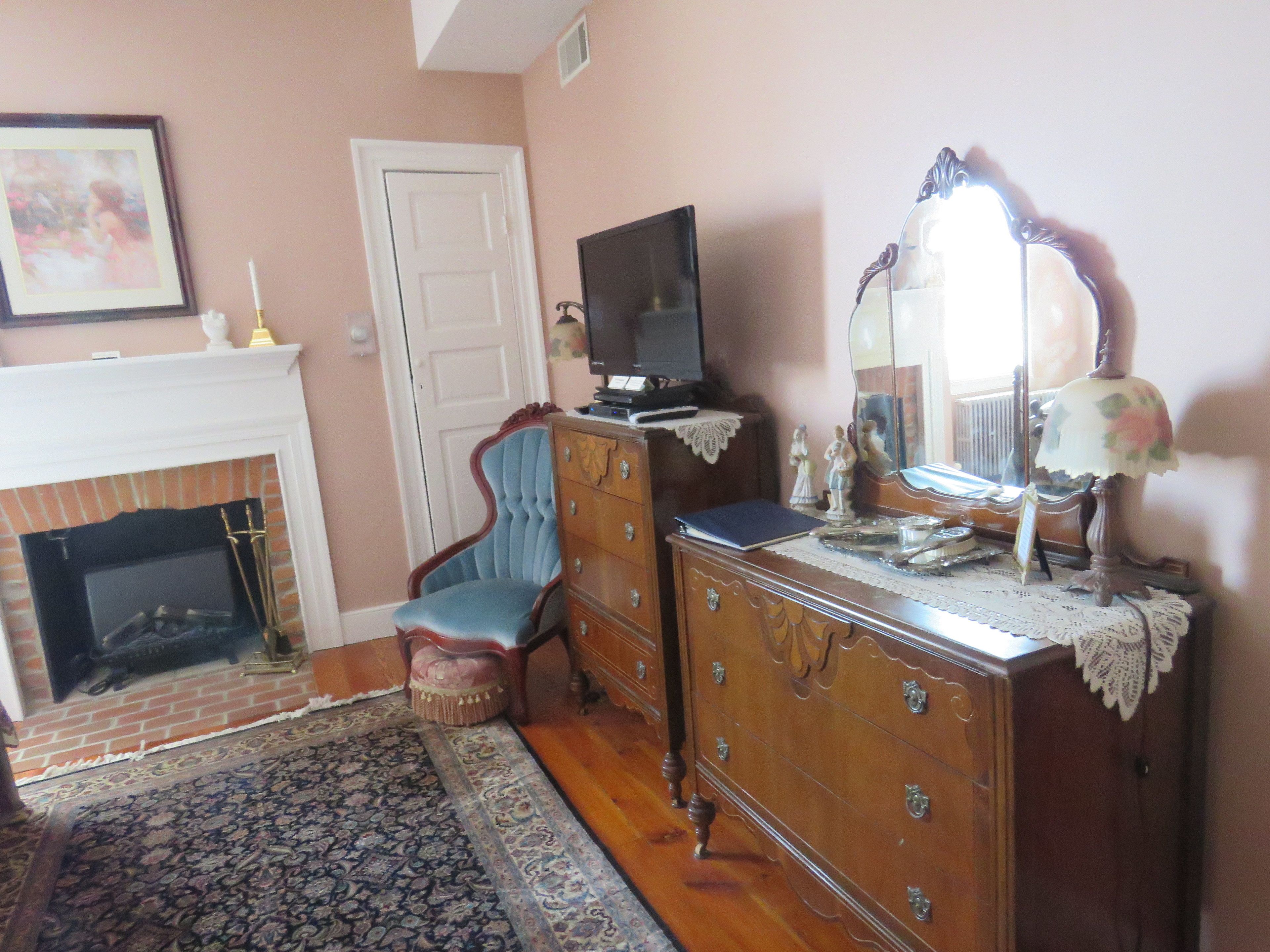 A room with a fireplace, a television on a dresser, a chair, and a patterned rug.