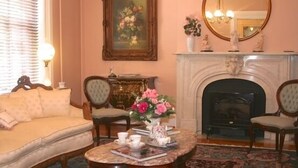 A living room with a beige sofa, two armchairs, a coffee table with books and a vase of flowers, a fireplace, and a bookshelf with various items. - The Swope Manor Bed & Breakfast (Gettysburg)