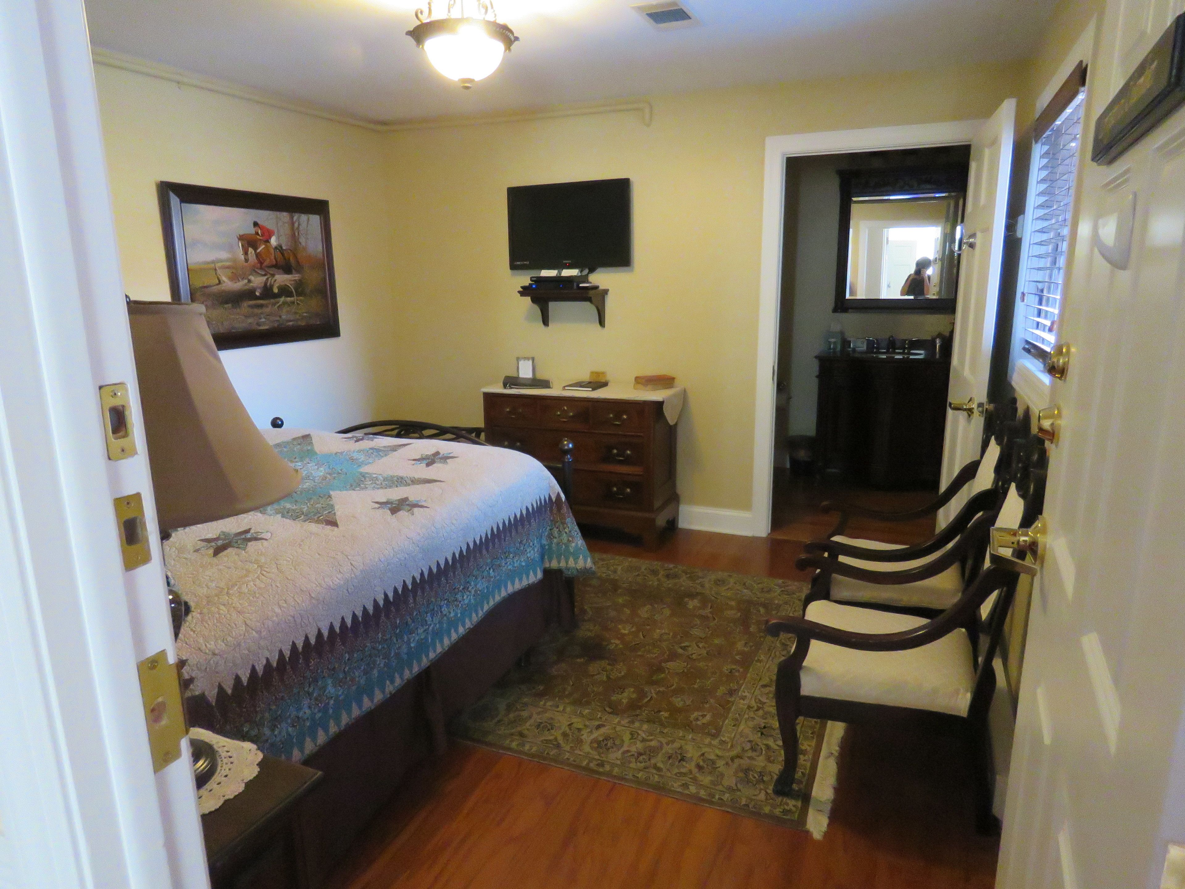 A bedroom with a bed, a dresser, a television, and a door leading to another room.