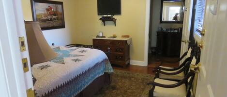 A bedroom with a bed, a dresser, a television, and a door leading to another room.
