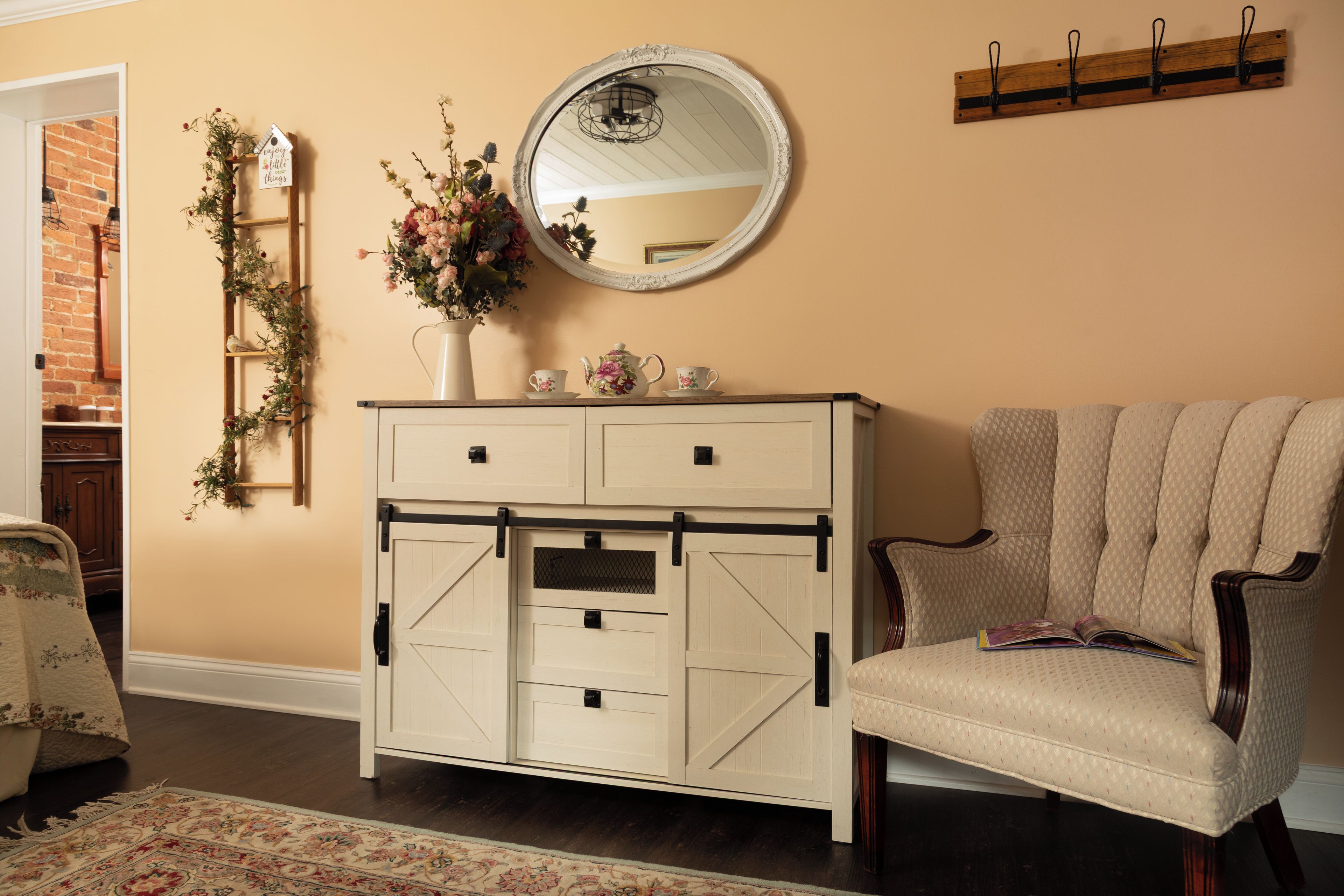 A room with a white dresser, a round mirror, a chair, and a wall-mounted coat rack.
