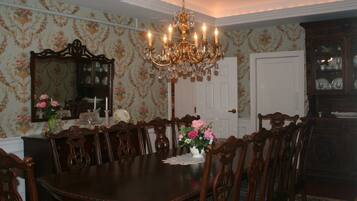 A dining room with a large wooden table surrounded by chairs, a chandelier, and floral wallpaper.