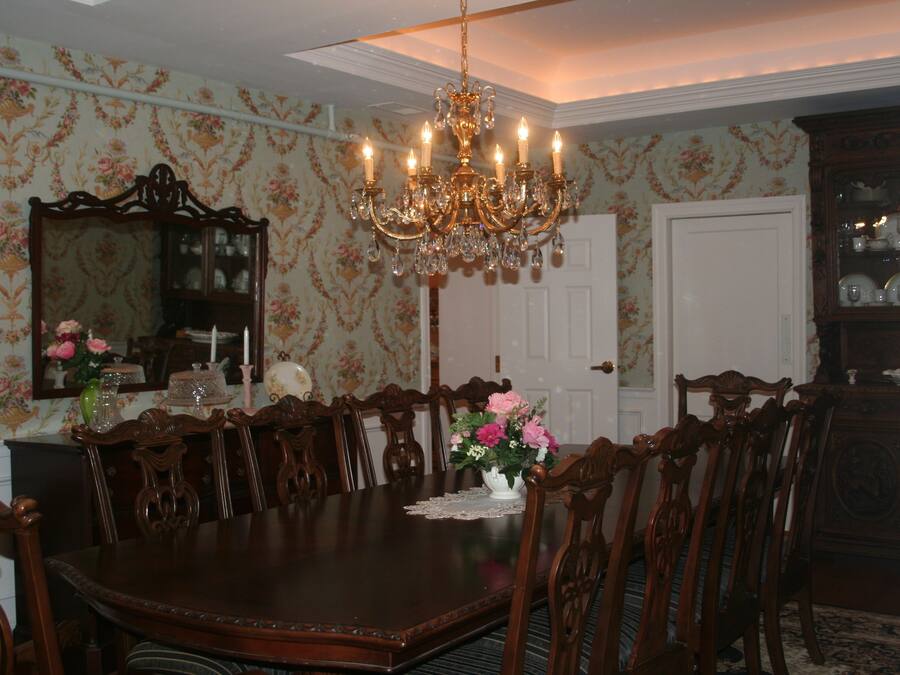 A dining room with a large wooden table surrounded by chairs, a chandelier, and floral wallpaper.