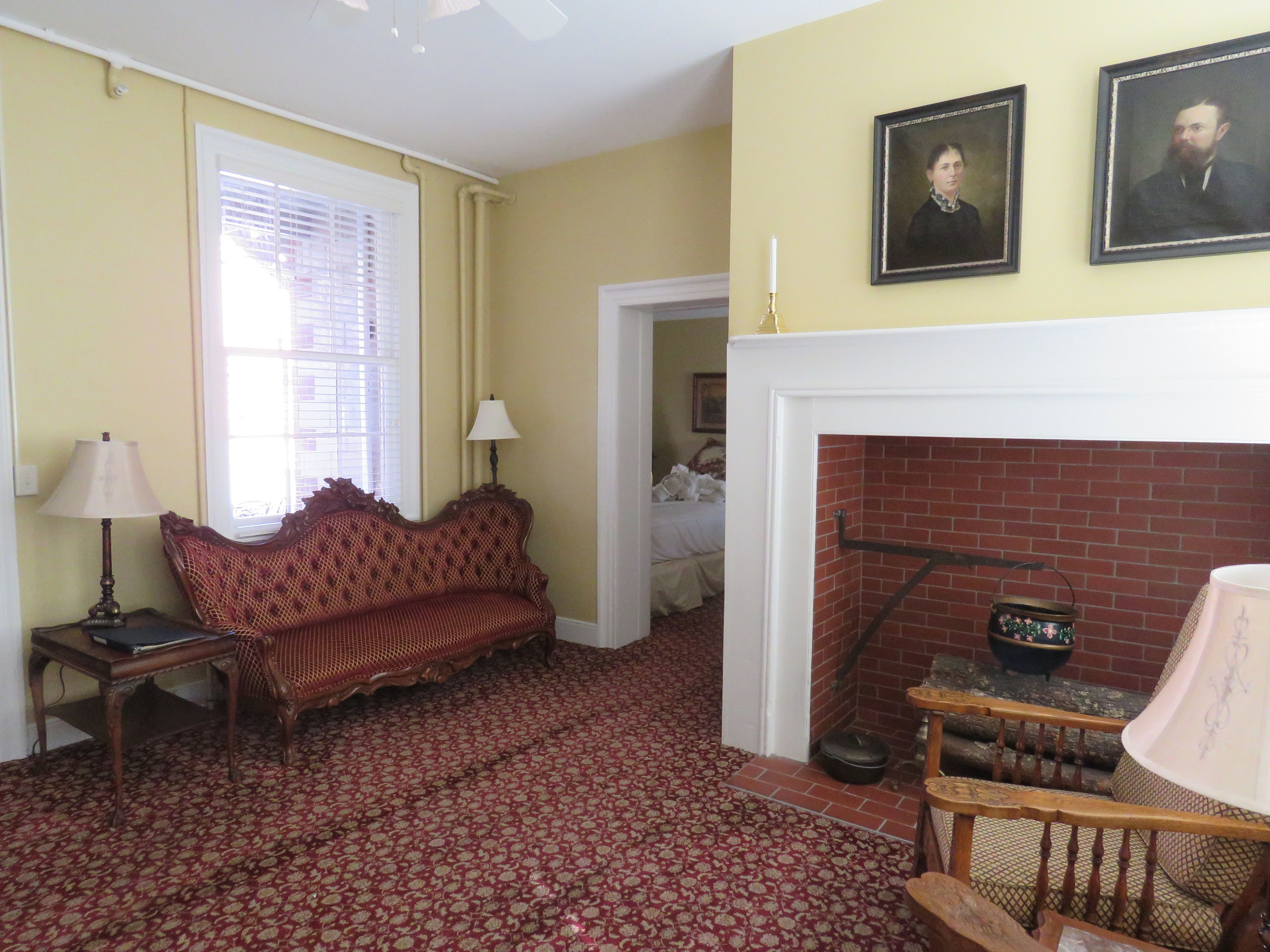 A room with a patterned carpet, a sofa, a lamp, a fireplace, and two framed portraits on the wall.