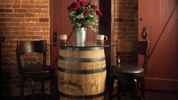 A rustic setting with a wooden barrel table, two chairs, a vase with red flowers, and a door in the background.