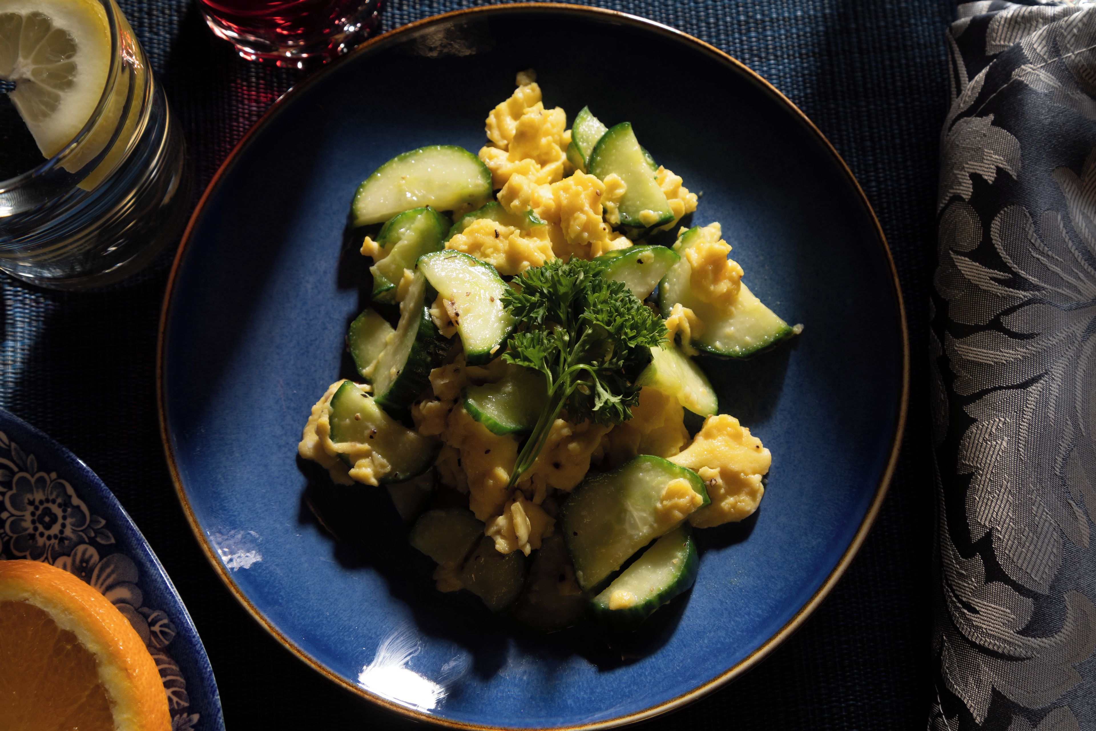 A plate of scrambled eggs with zucchini and parsley on a blue plate.