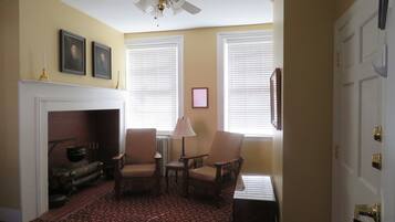 A room with a fireplace, two armchairs, a table, and a ceiling fan.