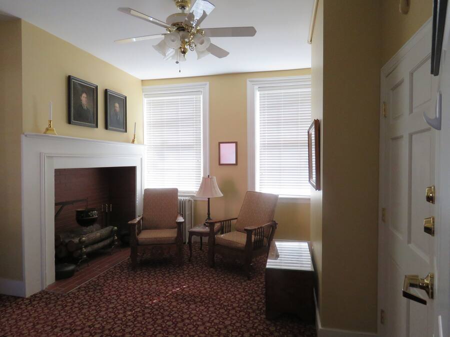 A room with a fireplace, two armchairs, a table, and a ceiling fan.