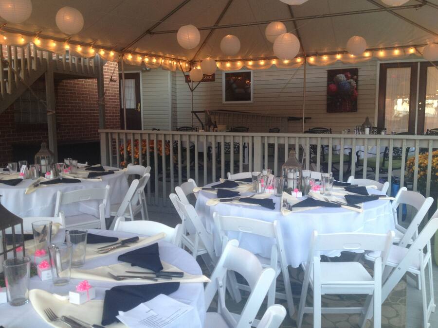 An outdoor dining area with white tables and chairs, string lights, and lanterns.