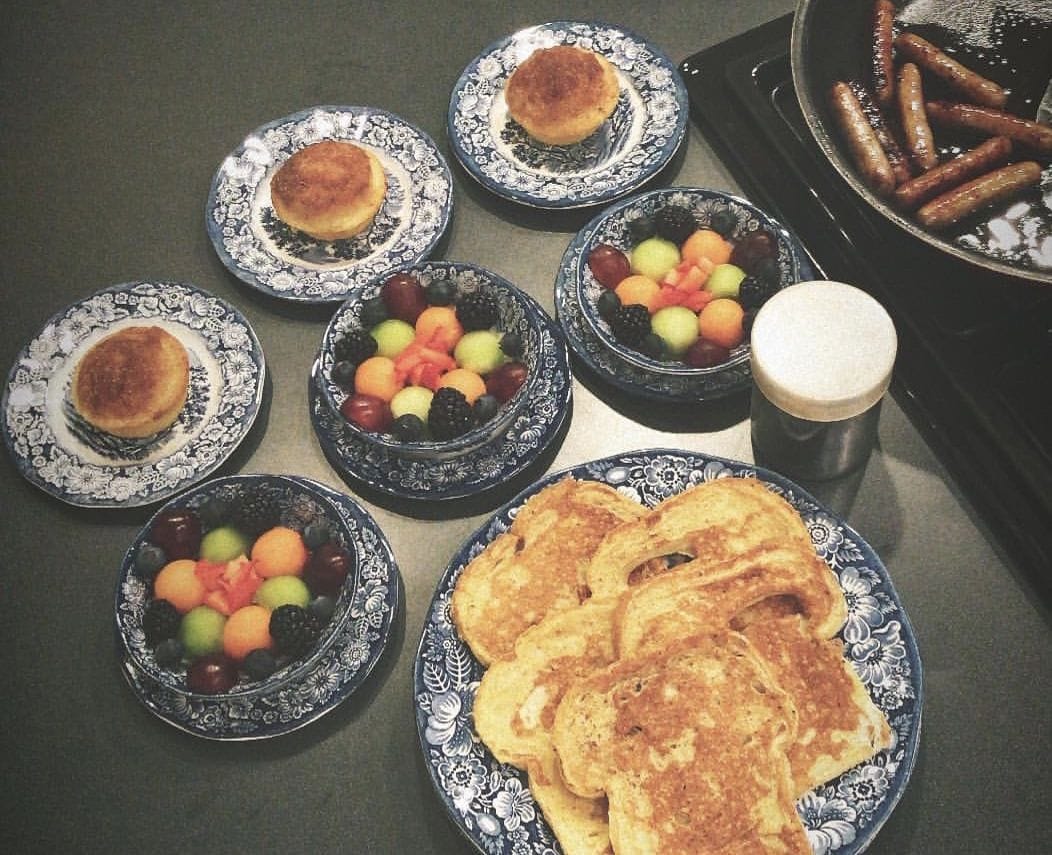 Una mesa con platos de tortitas, fruta, salchichas y una taza.