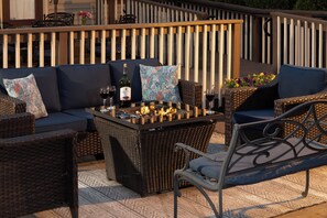 An outdoor seating area with wicker furniture, a fire feature, and a bottle of wine.