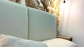 A bed with a stone wall behind it, a bedside lamp, and a pillow with embroidered text.