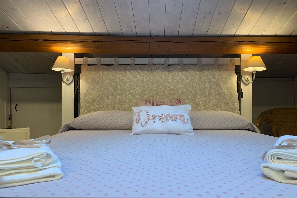 A bedroom with a bed, two bedside lamps, a floral-patterned headboard, and a pillow with "Dream" embroidered on it.