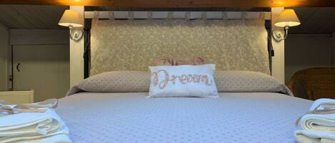 A bedroom with a bed, two bedside lamps, a floral-patterned headboard, and a pillow with "Dream" embroidered on it.
