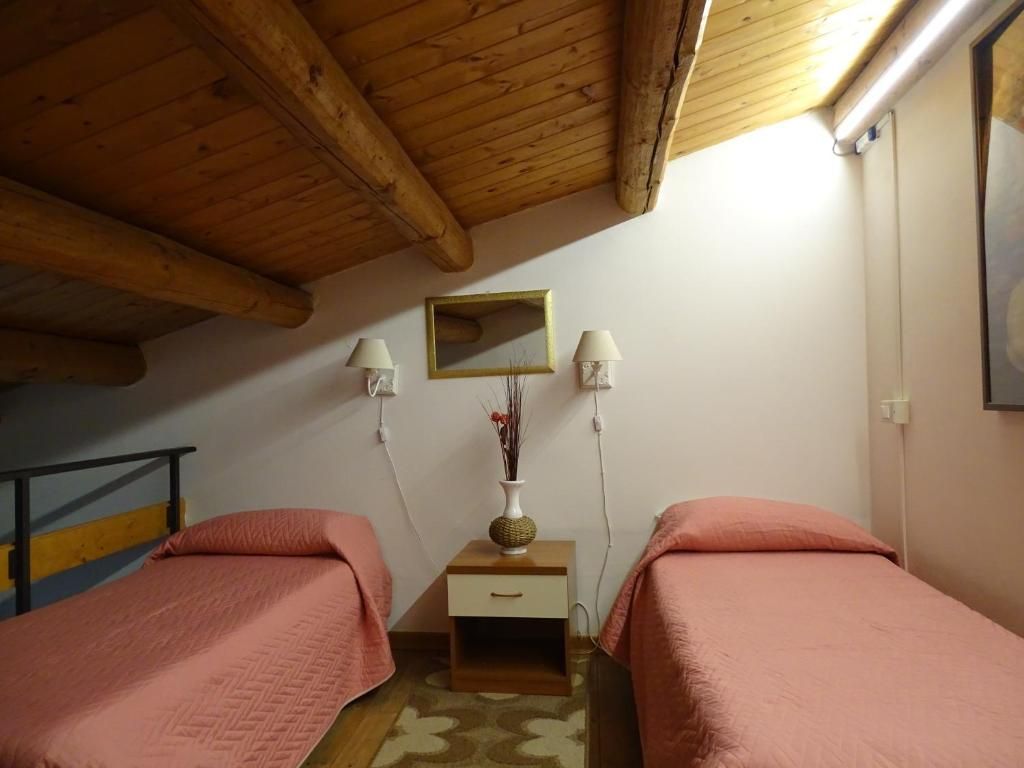 Una habitación con dos camas, vigas de madera en el techo, una mesita con un florero y un espejo en la pared.