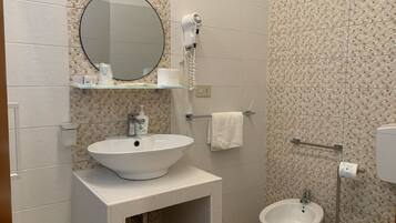 A bathroom with a white sink, a round mirror, a handheld showerhead, a toilet, and a bidet.