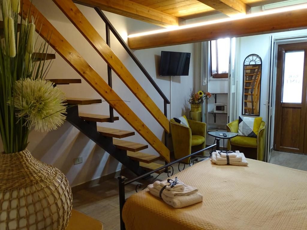 A hotel room with a wooden staircase, a flat-screen TV, a small table with a vase, and a bed with towels.