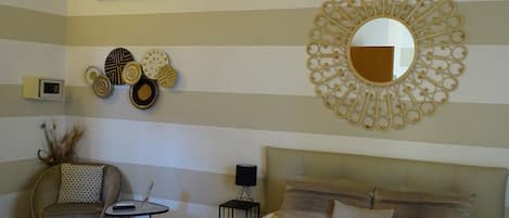 Une chambre à coucher comprenant un lit, une chaise, une petite table, un climatiseur fixé au mur, des assiettes décoratives et un miroir.