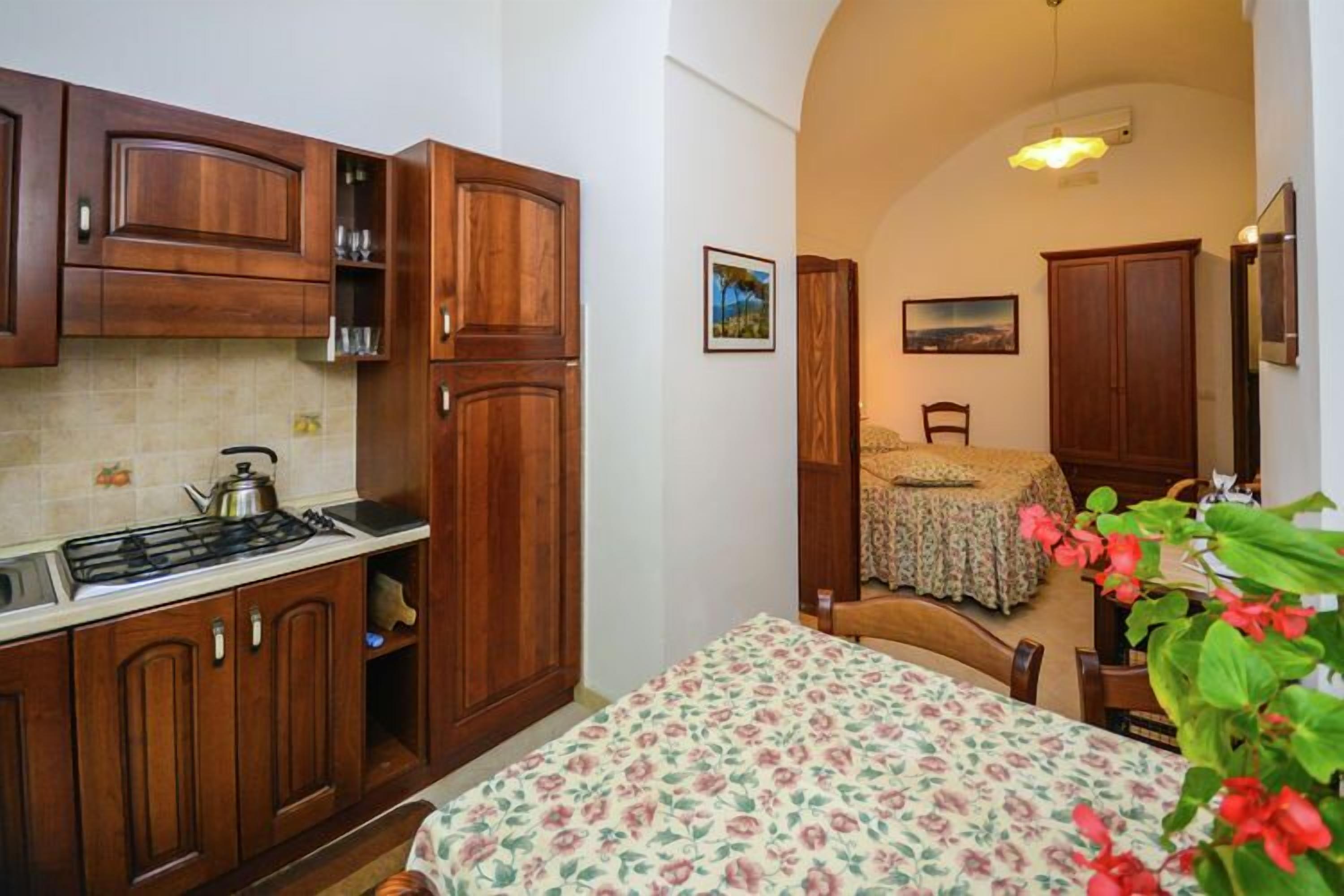 A compact kitchen with wooden cabinets, a gas stove, and a dining area with a floral tablecloth.