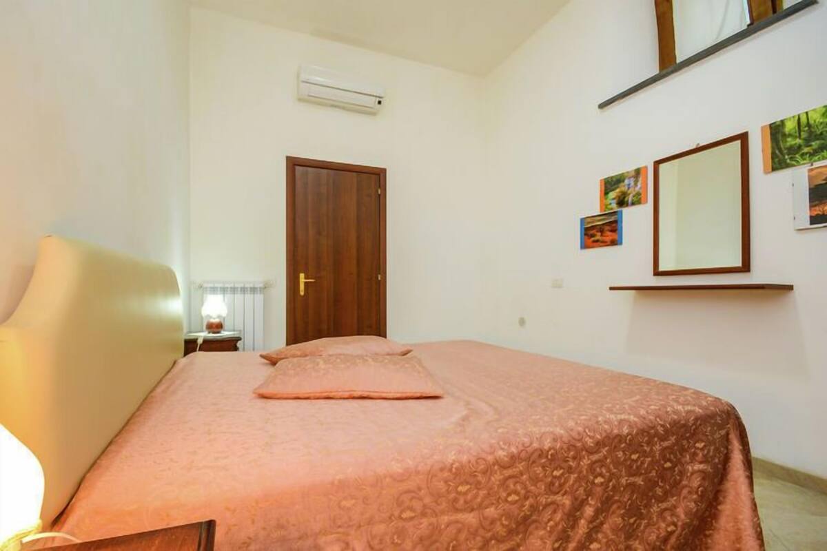 A bedroom with a bed, a nightstand, a lamp, a door, and a wall-mounted shelf with pictures.