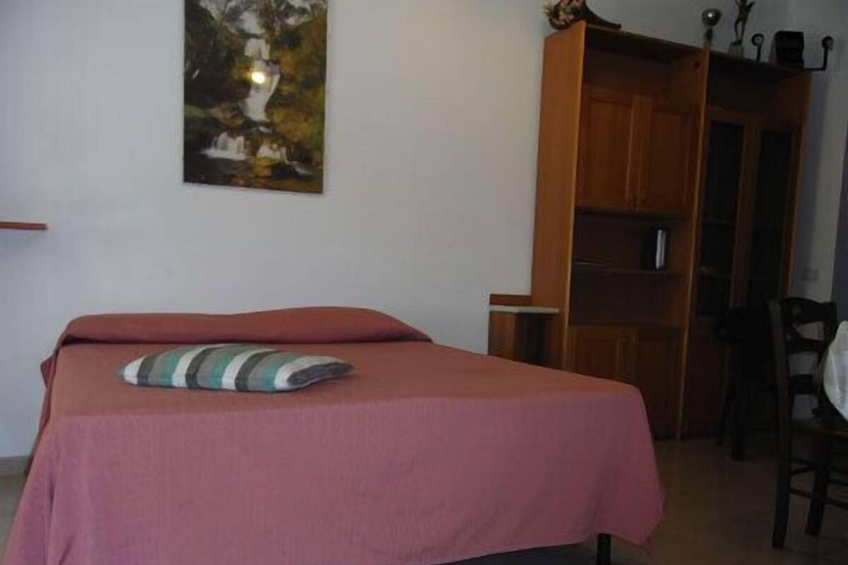 A bedroom with a bed, a wooden wardrobe, and a painting on the wall.