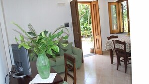 A room with a computer desk, a green sofa, a large green plant, and a dining area with a table and chairs. - Casale Nunziatina (Sorrento)