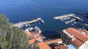 A coastal marina with boats docked, a pier extending into the water, and buildings with red-tiled roofs. - Casale Nunziatina (Sorrento)