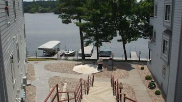A view of a lakeside walkway leading to a dock with boats, surrounded by trees and a building.