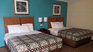A hotel room with two beds, each with patterned bedding, wooden headboards, and framed pictures on the walls.