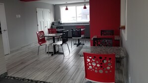 A modern kitchen with white cabinets, a microwave, and a dining area with red chairs and a table.
