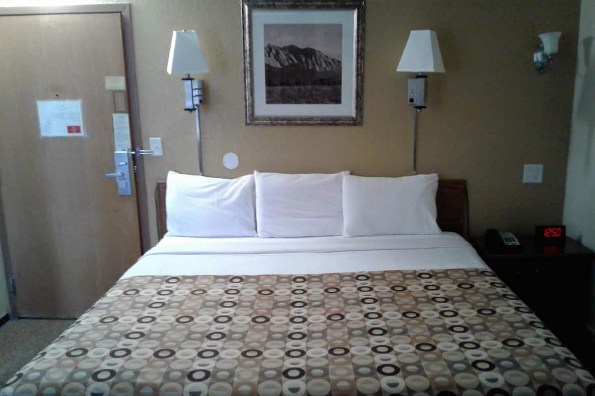A hotel room with a bed, two wall-mounted lamps, a framed picture, and a nightstand with a phone and alarm clock.