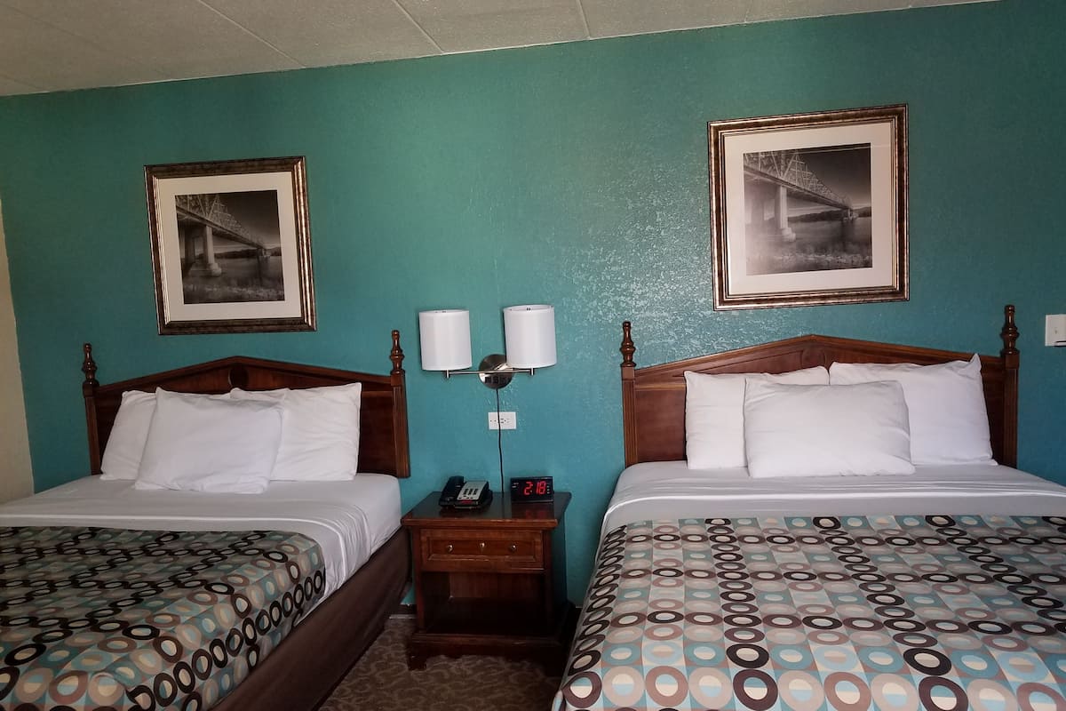 A hotel room with two beds, each with a patterned bedspread, a wooden headboard, and a nightstand with a phone and a digital clock.