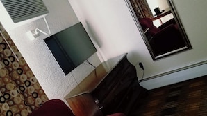 A room with a red armchair, a flat-screen TV, a dresser, a mirror, and a patterned rug.