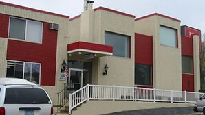 A multi-story building with a red and beige facade, a white fence, and a flag.