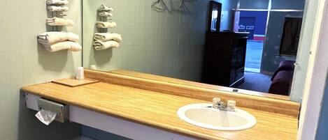 A bathroom with a wooden vanity, a white sink, and a mirror reflecting a door and a hallway.