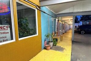 Fila de habitaciones de motel con cartel de aviso de servicio, una bandera y plantas en macetas.
