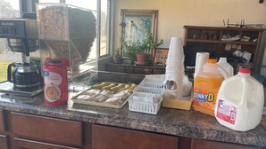 A kitchen counter with a coffee maker, a carton of coffee creamer, a tray of sliced bananas, a sugar container, a stack of paper cups, a jug of Sunny D, and a gallon of milk. - Gray Plaza Motel Benton Rend Lake I-57 (Benton)