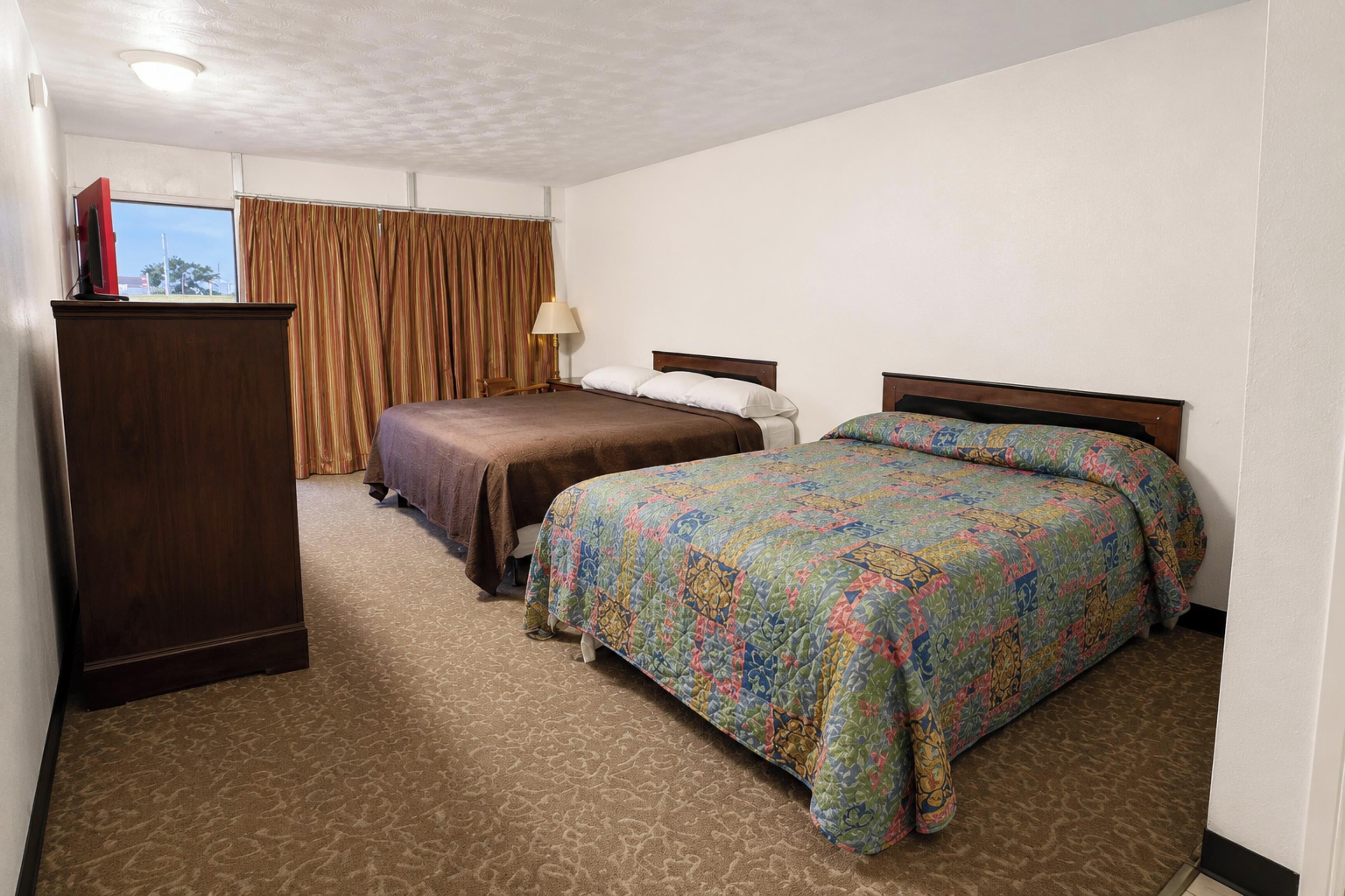 Habitación de hotel con dos camas, un escritorio y una ventana con cortinas.